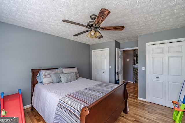 bedroom featuring ceiling fan, multiple closets, hardwood / wood-style flooring, and a textured ceiling