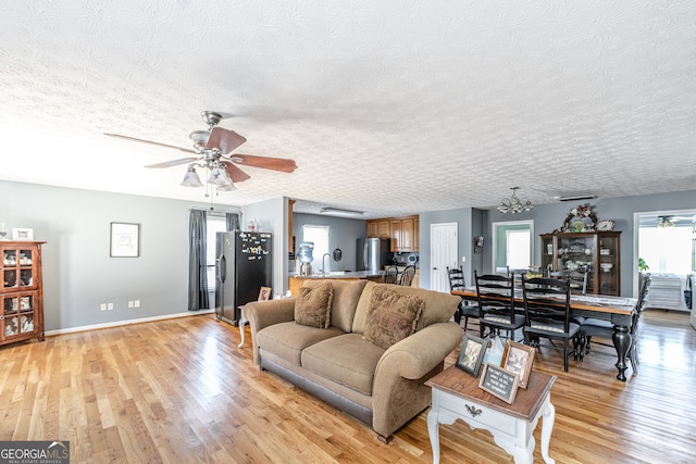 living room featuring a textured ceiling, light hardwood / wood-style floors, ceiling fan with notable chandelier, and sink