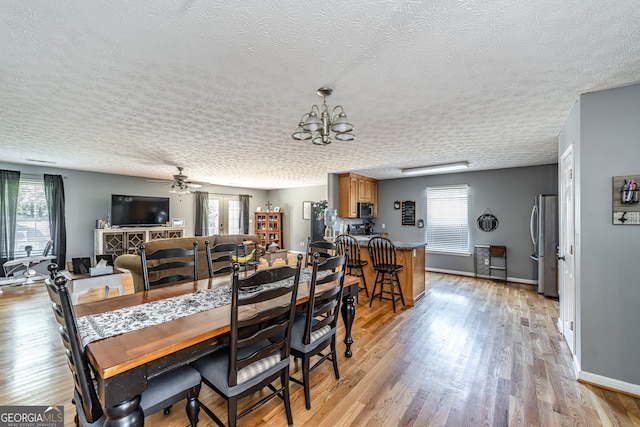 dining area with light wood-type flooring, ceiling fan with notable chandelier, a textured ceiling, and a healthy amount of sunlight