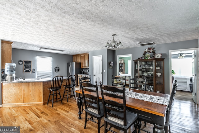 dining area featuring light wood-type flooring, sink, an inviting chandelier, and a textured ceiling