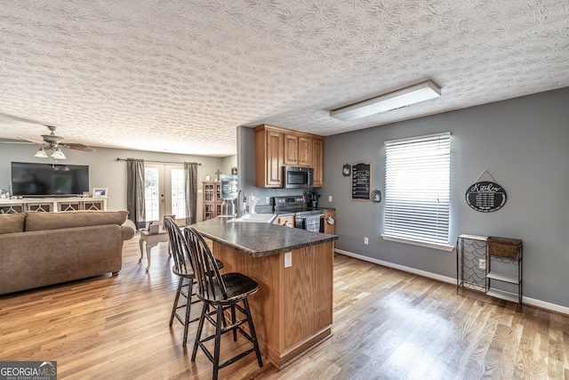 kitchen featuring light hardwood / wood-style flooring, a breakfast bar area, range with electric cooktop, and a textured ceiling