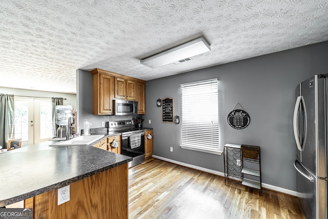 kitchen with sink, light wood-type flooring, french doors, stainless steel appliances, and kitchen peninsula