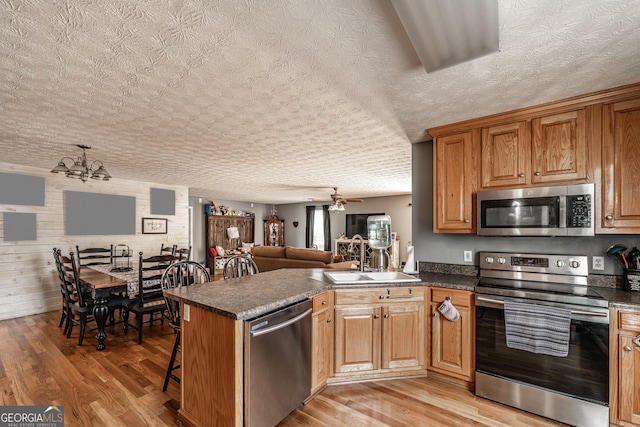 kitchen featuring light hardwood / wood-style floors, ceiling fan with notable chandelier, a textured ceiling, stainless steel appliances, and kitchen peninsula