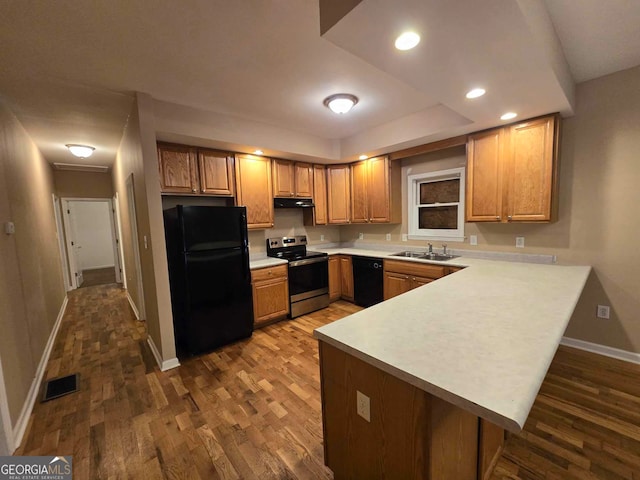 kitchen with sink, kitchen peninsula, black appliances, a kitchen breakfast bar, and dark hardwood / wood-style floors