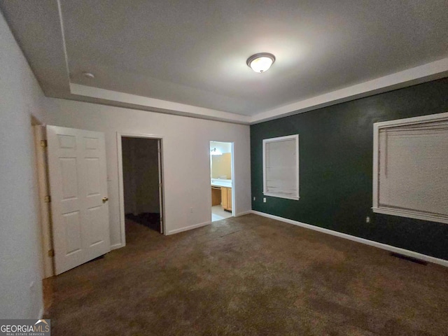 unfurnished bedroom with ensuite bath, dark carpet, and a raised ceiling