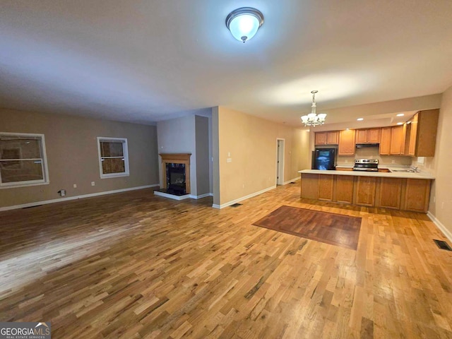 kitchen featuring black refrigerator, light hardwood / wood-style floors, kitchen peninsula, an inviting chandelier, and decorative light fixtures