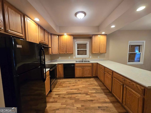 kitchen with black appliances, a raised ceiling, sink, kitchen peninsula, and light hardwood / wood-style flooring