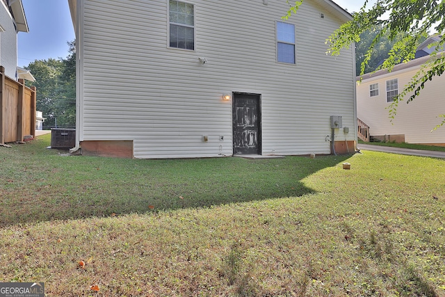 rear view of property with central AC unit and a lawn