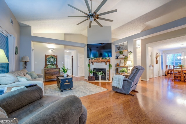 living room with lofted ceiling, ceiling fan with notable chandelier, hardwood / wood-style floors, and a tile fireplace