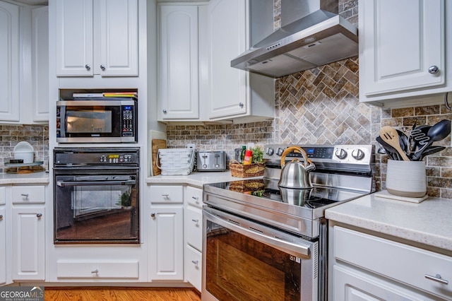 kitchen featuring light wood-type flooring, appliances with stainless steel finishes, tasteful backsplash, wall chimney range hood, and white cabinets