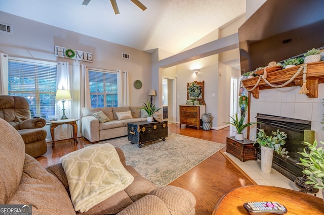 living room featuring a healthy amount of sunlight, light wood-type flooring, lofted ceiling, a tile fireplace, and ceiling fan