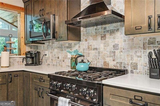 kitchen with range with two ovens, dark brown cabinetry, wall chimney exhaust hood, and backsplash