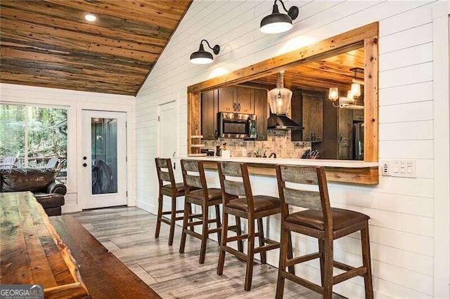 bar featuring lofted ceiling, light hardwood / wood-style flooring, pendant lighting, and wood ceiling