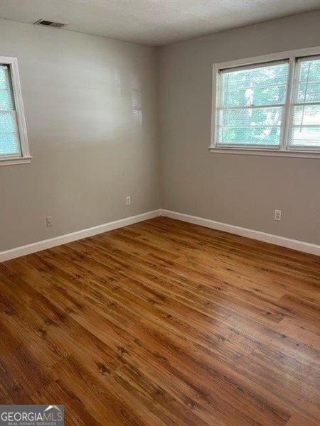 spare room featuring a textured ceiling, wood finished floors, visible vents, and baseboards