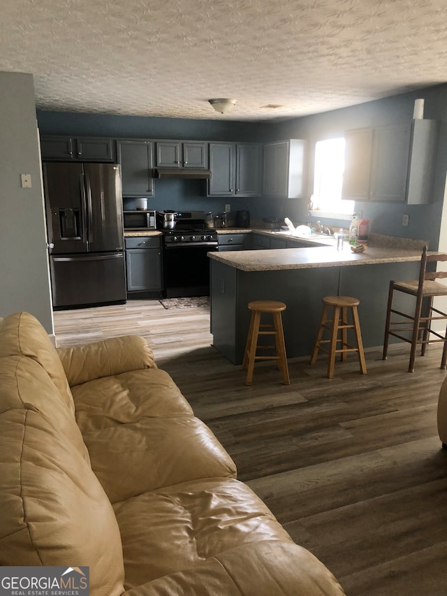 kitchen featuring a breakfast bar, a textured ceiling, kitchen peninsula, stainless steel appliances, and hardwood / wood-style floors