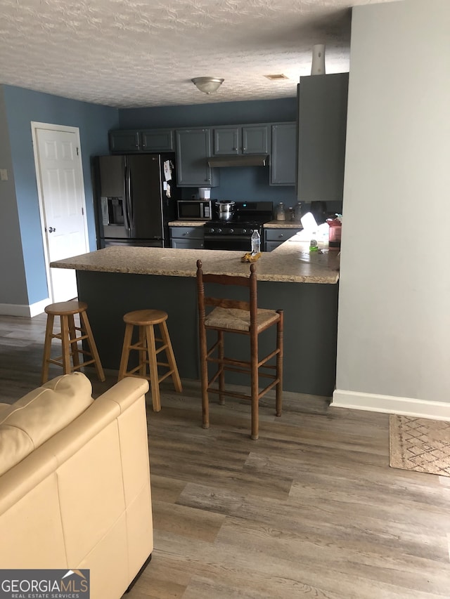 kitchen with a breakfast bar, kitchen peninsula, a textured ceiling, black appliances, and hardwood / wood-style floors