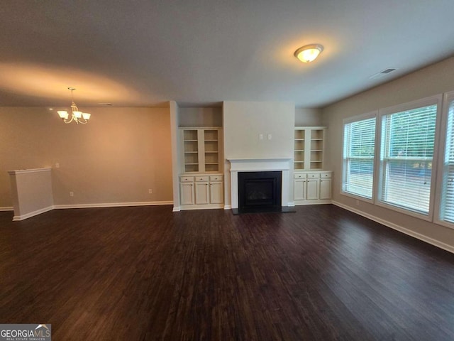 unfurnished living room with built in features, dark wood-type flooring, and a chandelier