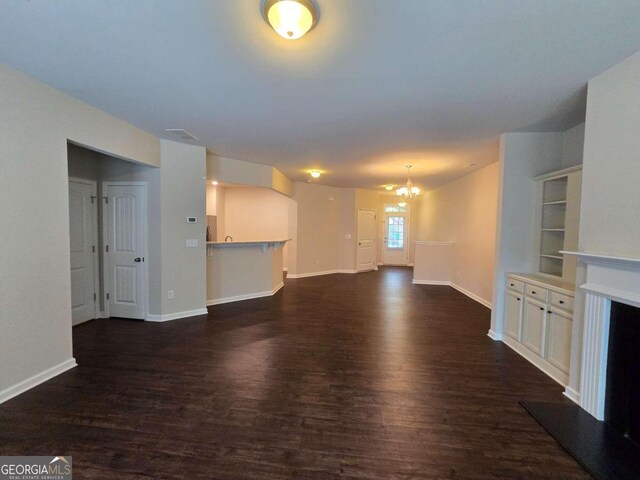 unfurnished living room with dark wood-style floors, a fireplace with raised hearth, a notable chandelier, and baseboards