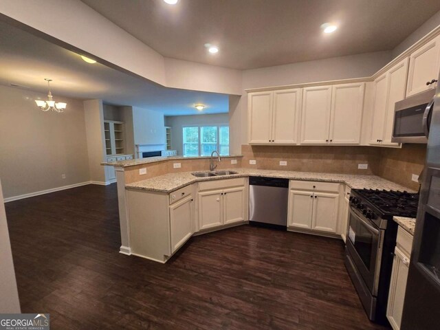 kitchen featuring appliances with stainless steel finishes, a peninsula, light stone countertops, white cabinetry, and a sink