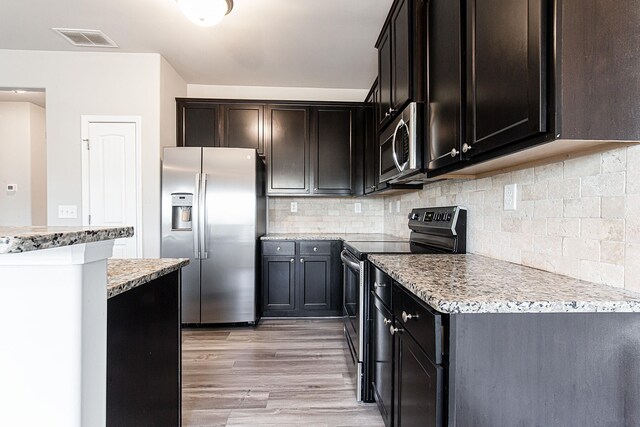 kitchen featuring appliances with stainless steel finishes, dark brown cabinets, light wood-type flooring, and tasteful backsplash