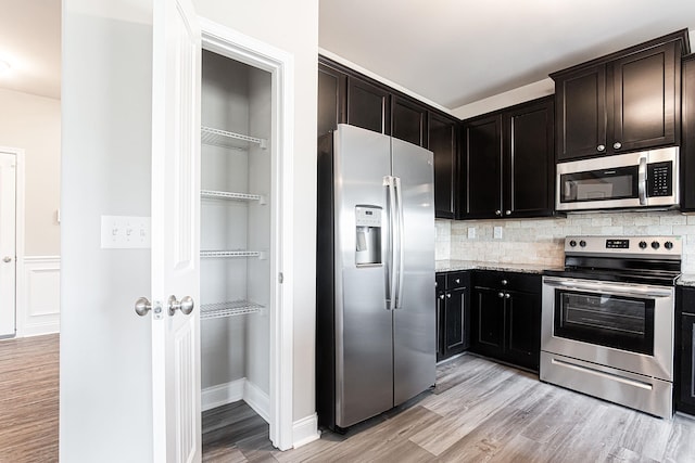 kitchen with stainless steel appliances, decorative backsplash, light wood-type flooring, and light stone countertops