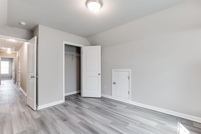 unfurnished bedroom featuring a closet, lofted ceiling, and light hardwood / wood-style flooring