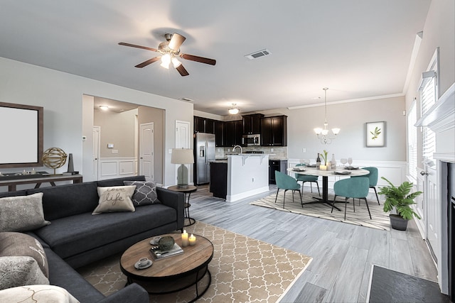 living room with light hardwood / wood-style floors, ceiling fan with notable chandelier, and ornamental molding