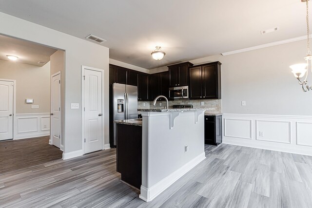 kitchen with decorative backsplash, light stone countertops, an island with sink, stainless steel appliances, and pendant lighting