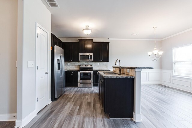 kitchen featuring stainless steel appliances, sink, light stone counters, wood-type flooring, and hanging light fixtures