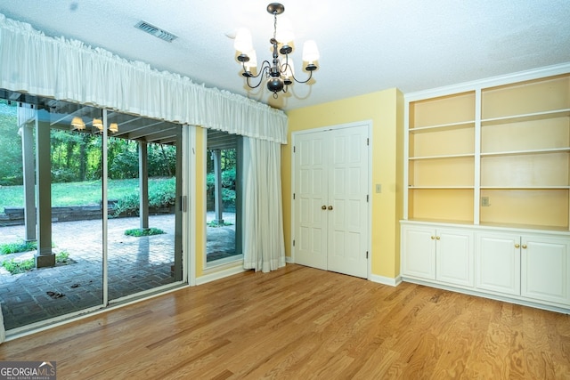 empty room with light hardwood / wood-style flooring, a textured ceiling, and an inviting chandelier