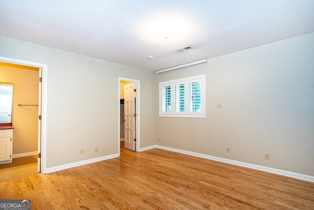 unfurnished bedroom with a textured ceiling, light hardwood / wood-style flooring, ensuite bath, and a walk in closet