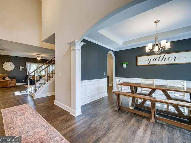 dining space featuring arched walkways, a tray ceiling, wainscoting, wood finished floors, and stairs