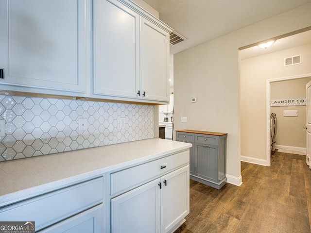 kitchen with baseboards, visible vents, dark wood-style floors, light countertops, and backsplash