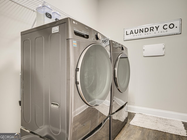 washroom with laundry area, washer and clothes dryer, baseboards, and wood finished floors