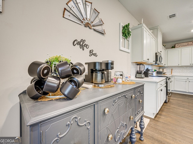 kitchen with stainless steel appliances, tasteful backsplash, light countertops, visible vents, and wood finished floors