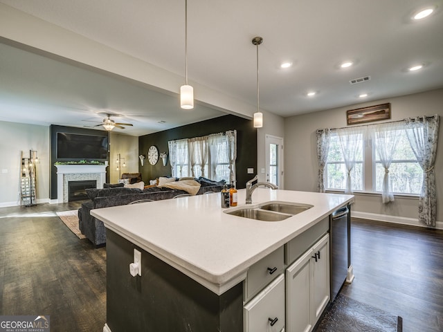 kitchen with visible vents, a tiled fireplace, an island with sink, a sink, and stainless steel dishwasher