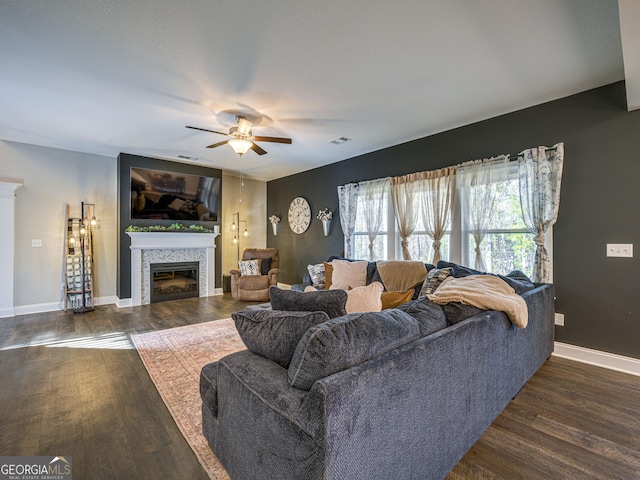 living area featuring visible vents, baseboards, a tiled fireplace, ceiling fan, and wood finished floors