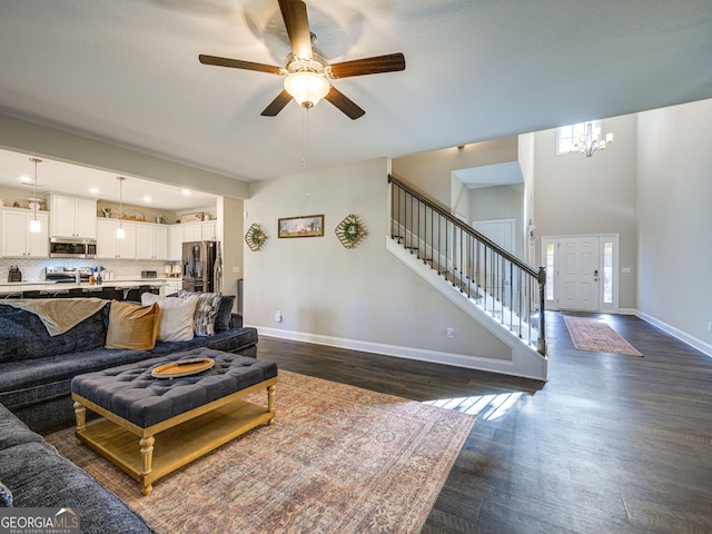 living room featuring ceiling fan with notable chandelier, dark wood finished floors, baseboards, and stairs