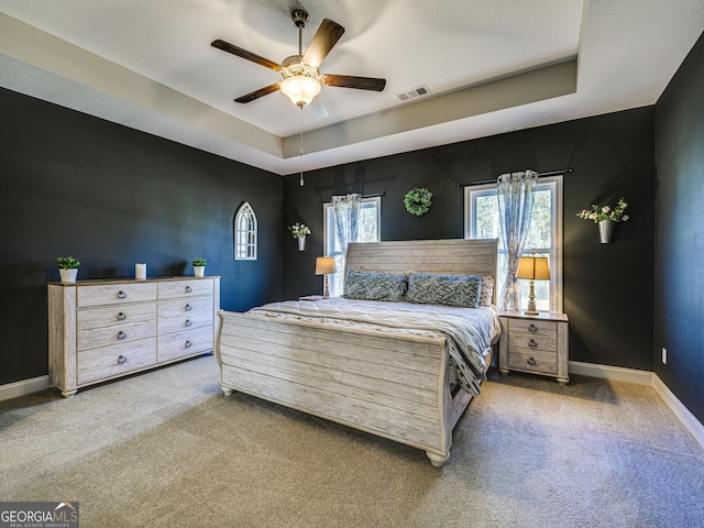 bedroom with a raised ceiling, visible vents, carpet flooring, ceiling fan, and baseboards