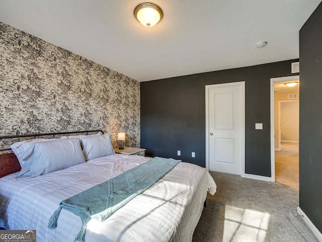 carpeted bedroom with an accent wall, visible vents, baseboards, and wallpapered walls