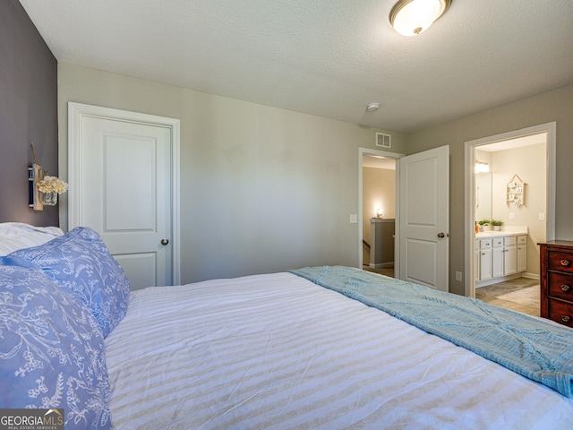 bedroom with ensuite bathroom, a textured ceiling, and visible vents