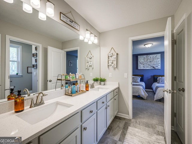 bathroom featuring ensuite bathroom, double vanity, a sink, and baseboards