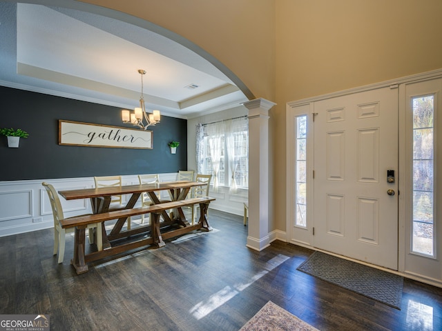 entryway with arched walkways, dark wood finished floors, a raised ceiling, an inviting chandelier, and wainscoting