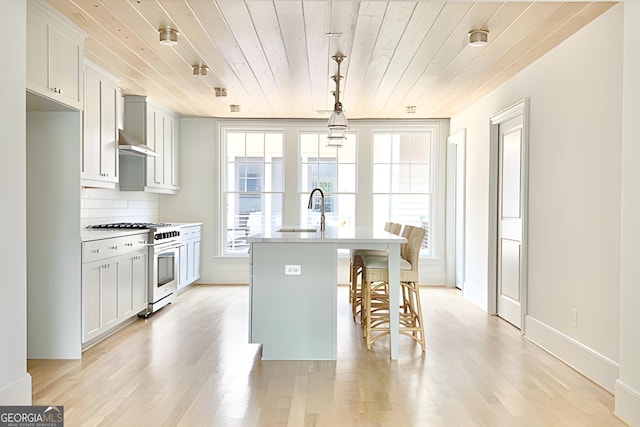 kitchen featuring a center island with sink, wooden ceiling, high end stainless steel range oven, and light hardwood / wood-style flooring