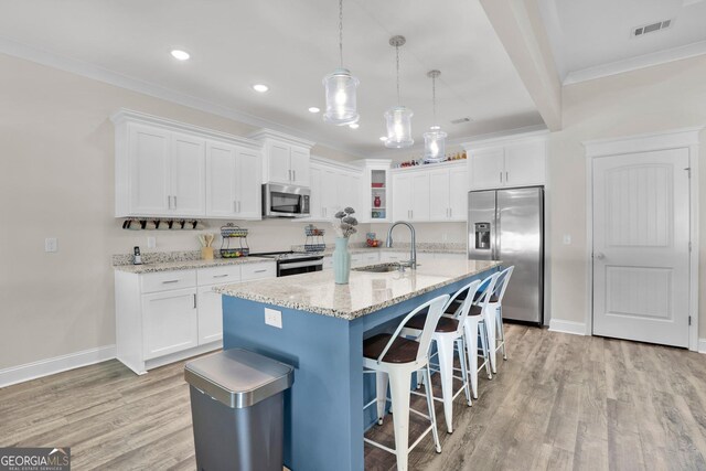 kitchen with ornamental molding, light hardwood / wood-style flooring, a kitchen island with sink, and stainless steel appliances