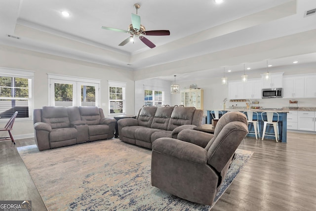 living room with ceiling fan, french doors, light hardwood / wood-style floors, and a tray ceiling