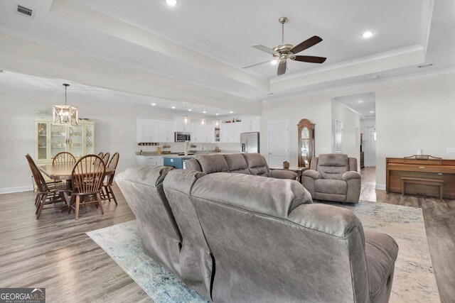 living room featuring a tray ceiling, light hardwood / wood-style floors, ceiling fan with notable chandelier, and crown molding