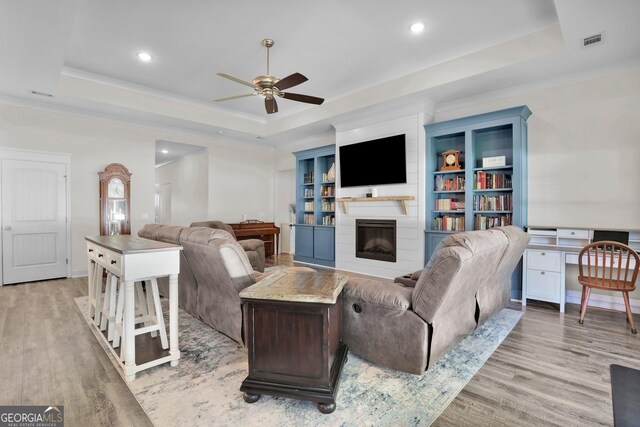 living room featuring ceiling fan, light wood-type flooring, crown molding, and a tray ceiling