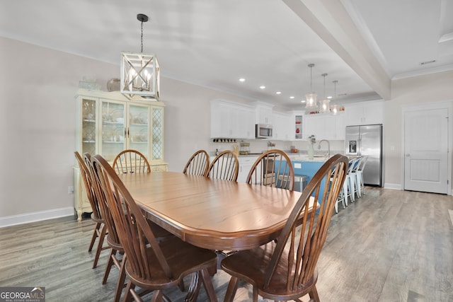 dining room with sink, light wood-type flooring, a notable chandelier, and beam ceiling