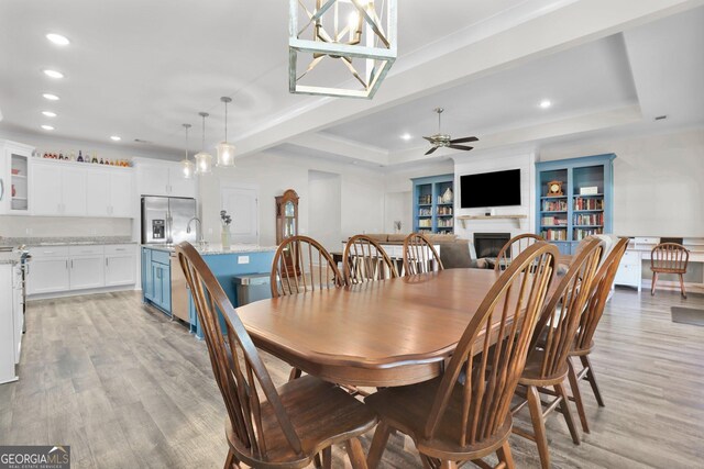 dining space with light wood-type flooring, built in shelves, ceiling fan, and a tray ceiling